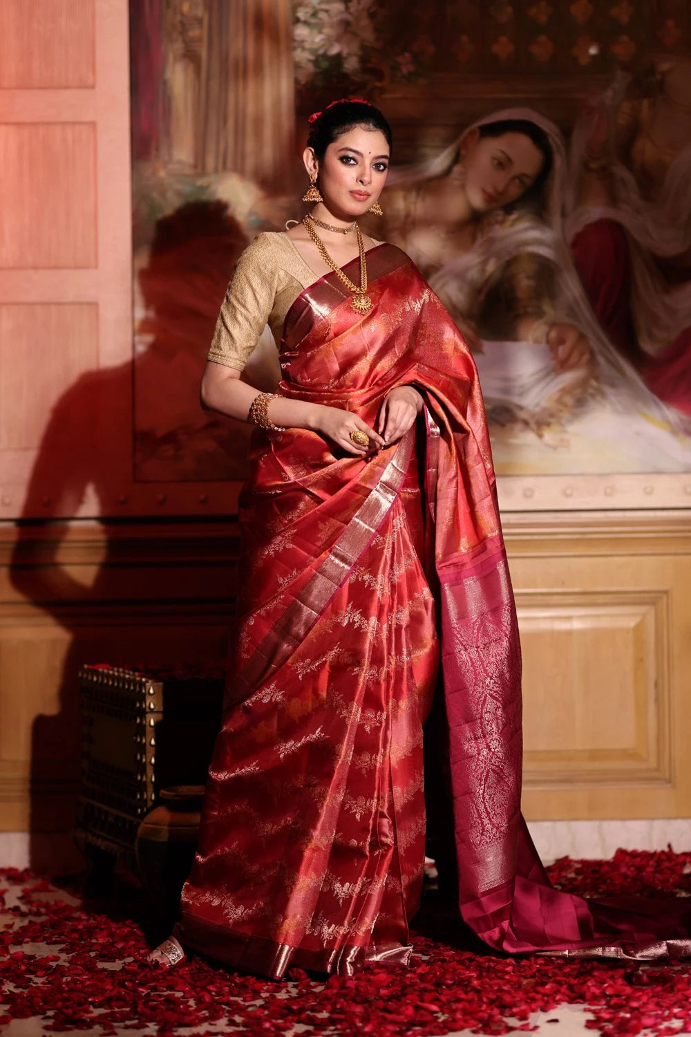 Woman in a red saree standing in front of a decorative wall.