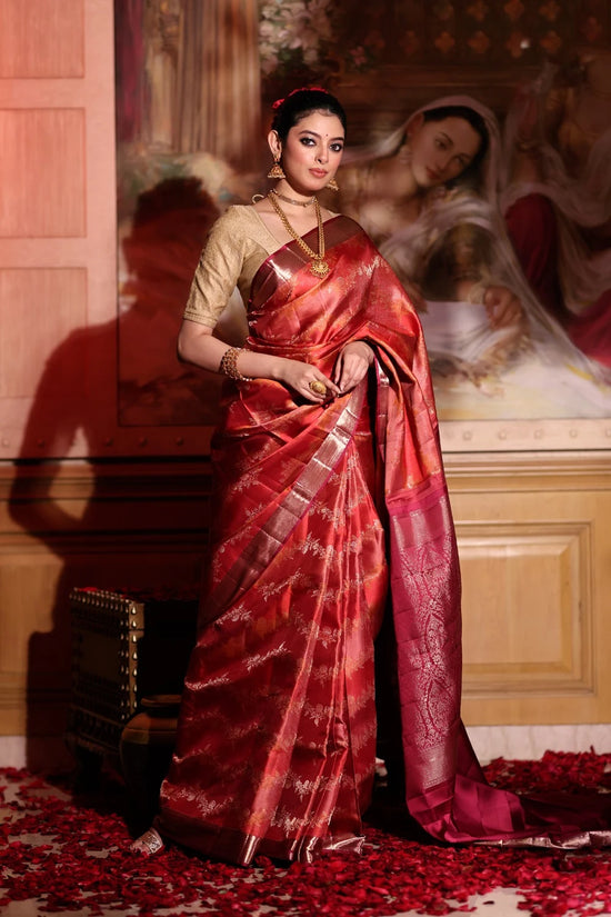 Woman in a red saree standing in front of a decorative wall.