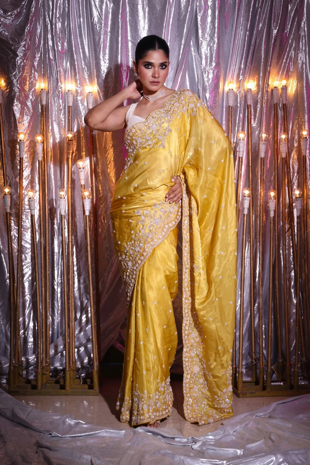 Woman in a yellow saree with silver embroidery against a decorative curtain background